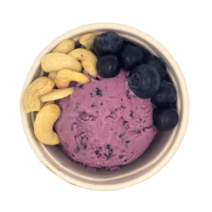 Scoop of blueberry ice cream in a cup surrounded by cashews and blueberries.